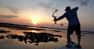 A man bowfishing with a sunrise in the background